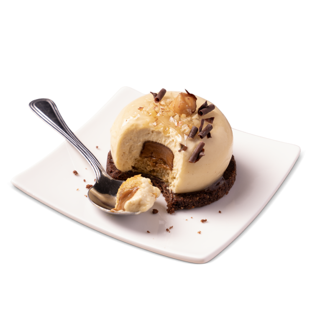 Desert cu mousse de caramel în formă de cupolă pe biscuit cu ciocolată, cu alune și fulgi de ciocolată, mușcat