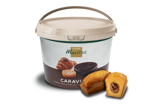 Găleată mare de cremă tartinabilă Master Martini Caravella lângă un mini tort cu cremă de ciocolată.