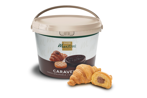 Găleată bej de cremă de ciocolată Caravel Master Martini alături de două croissante, unul umplut cu ciocolată.