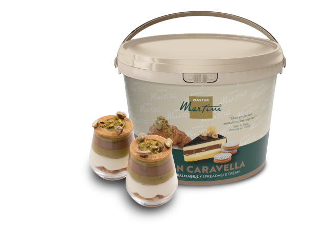 Găleată mare de cremă tartinabilă Master Martini lângă două pahare de desert cu cremă, ciocolată și fistic măcinat.