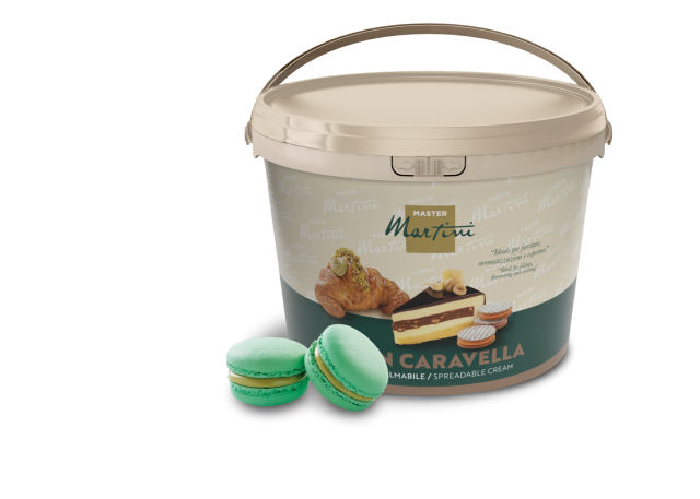 Cutie bej de cremă tartinabilă Master Martini cu imagini de patiserie, lângă două macarons verzi cu fistic.